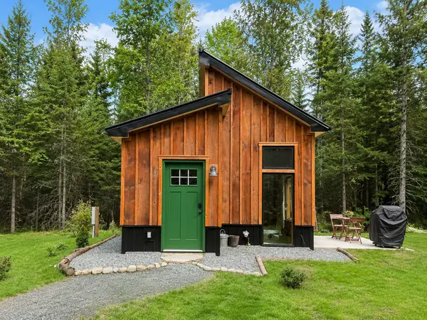 Front of the cabin with green door surrounded by green grass and evergreens