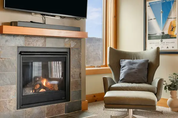 Gas fireplace lit beside a leather reading chair with mountain views