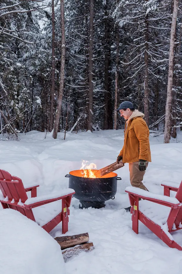Guest tending the fire pit at dusk with red Adirondack chairs