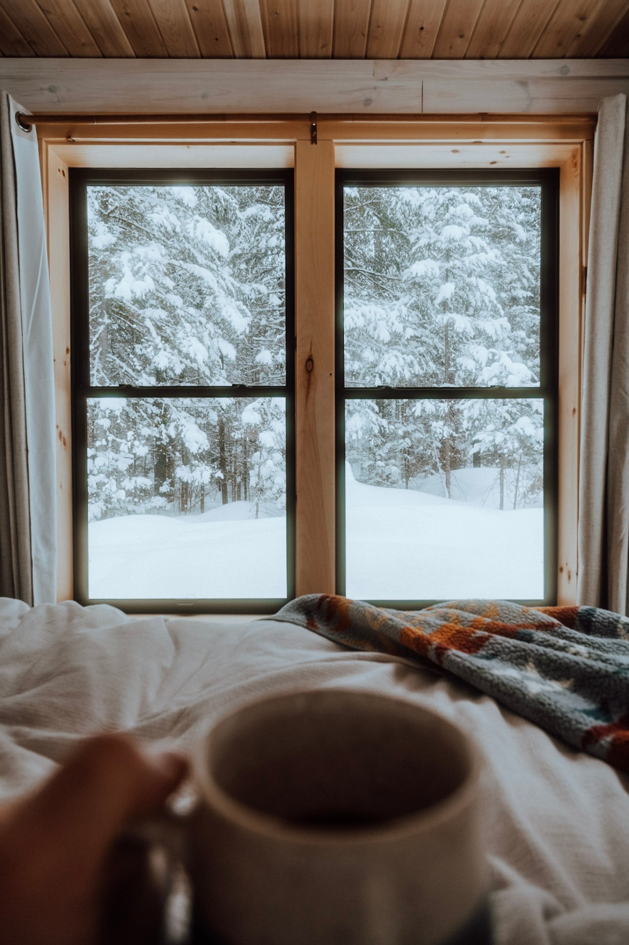Morning coffee in bed with snowy forest view through cabin window