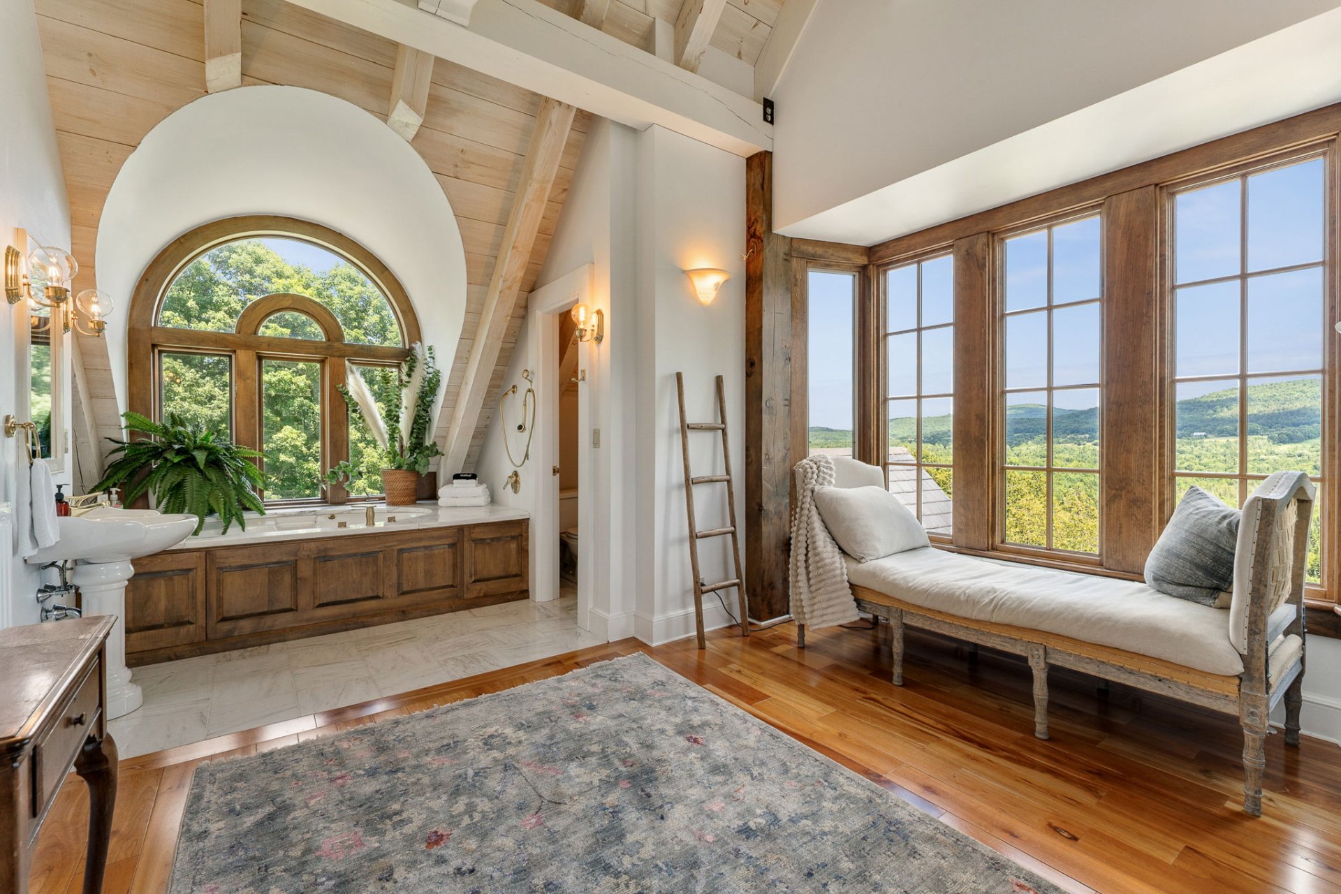 Primary bathroom with arched window, daybed, and Vermont mountain views