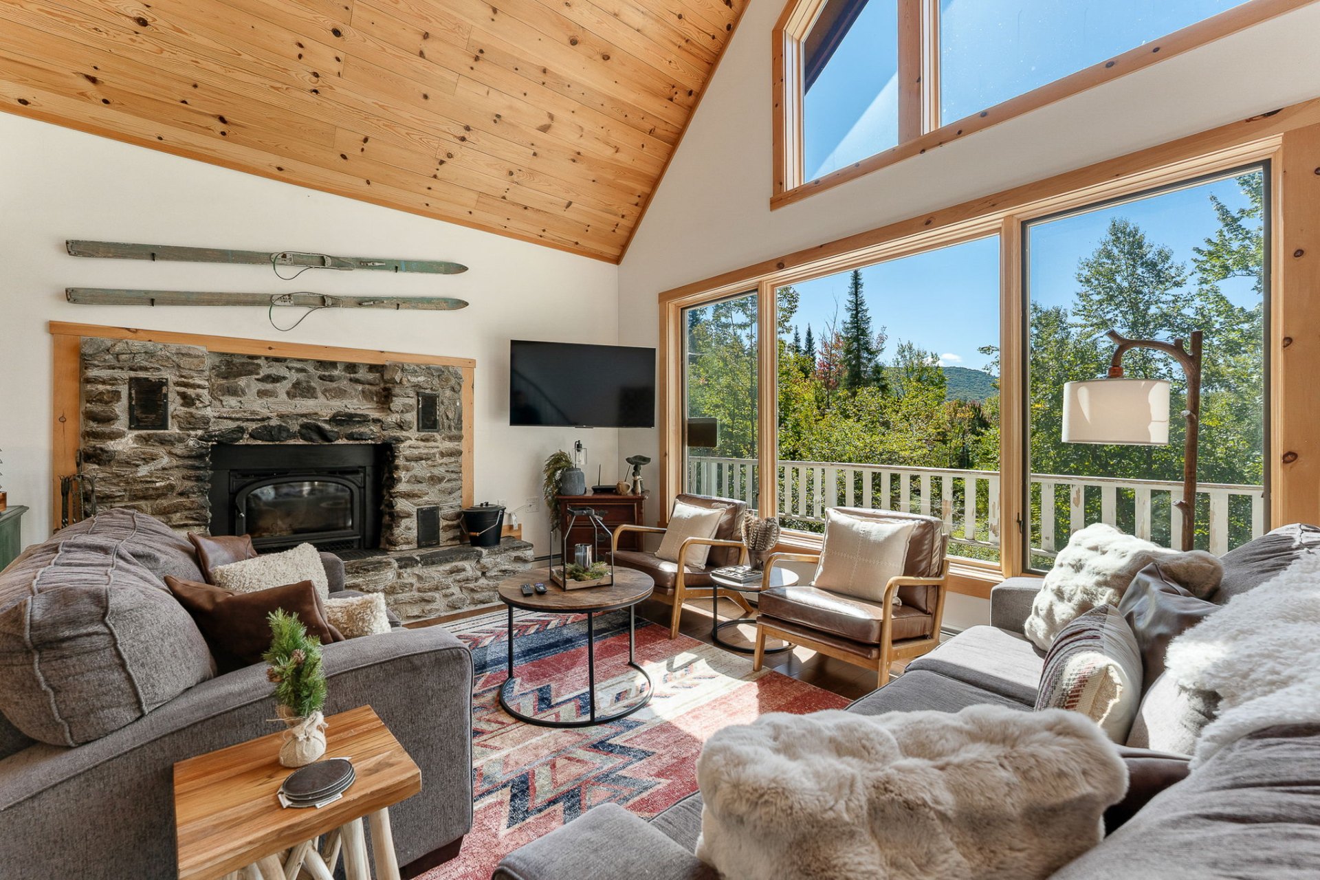 Open chalet living room with stone fireplace and mountain views through tall windows