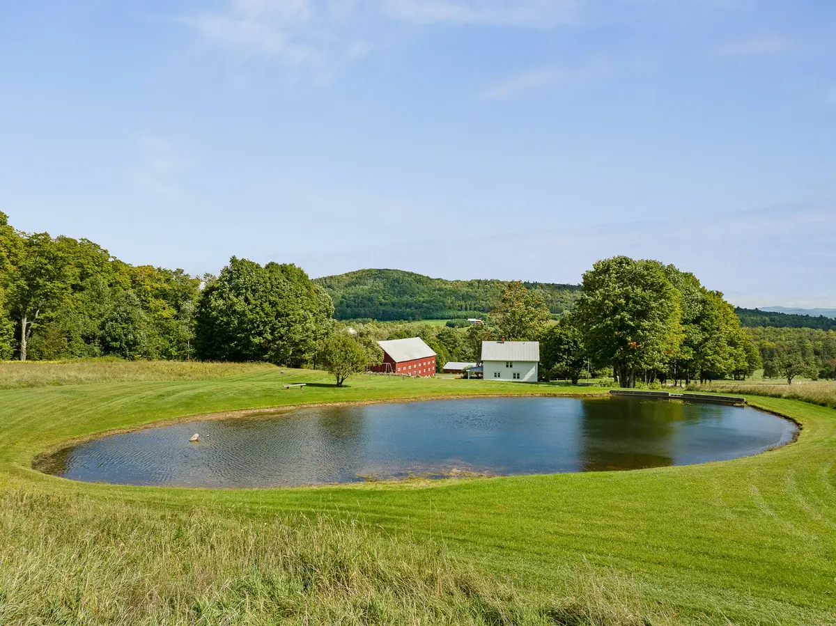 Private pond on a Vermont farm with rolling hills and a white farmhouse beyond